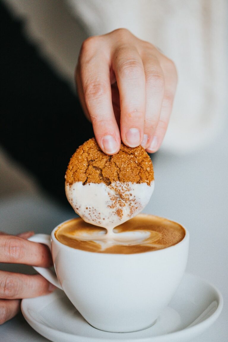 person holding white ceramic mug with brown and white liquid